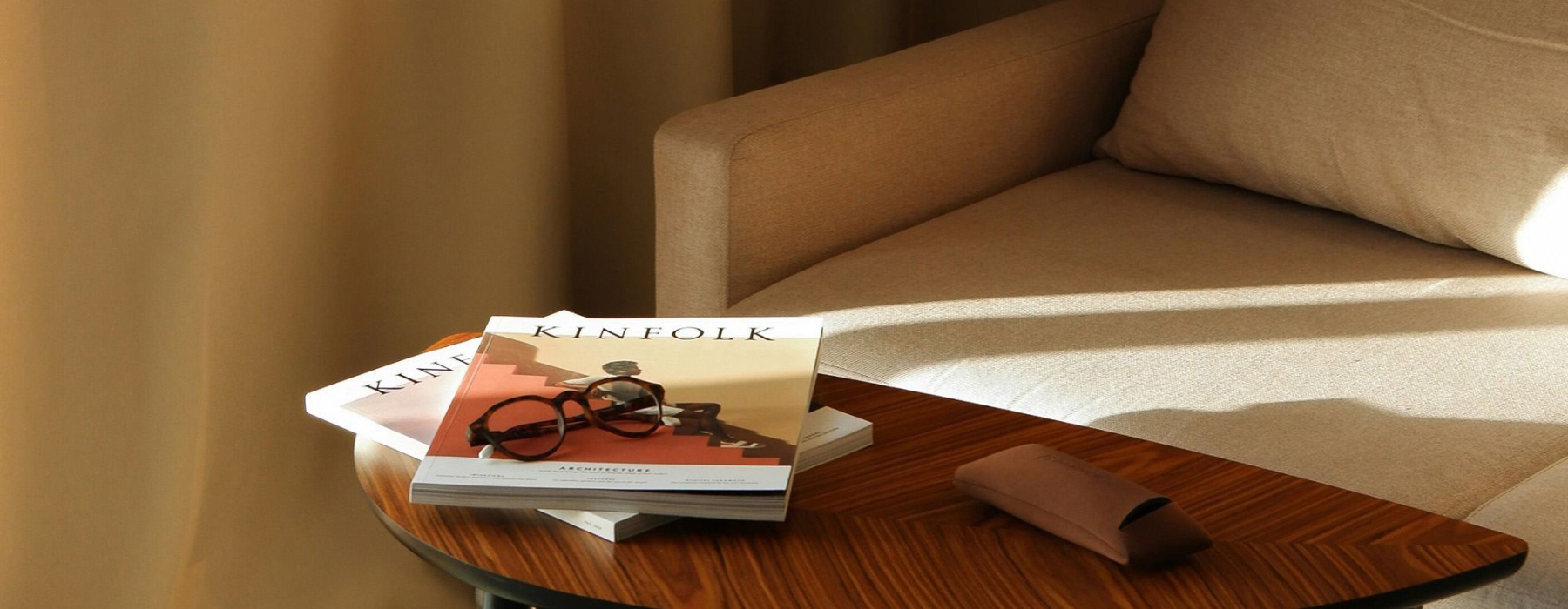 A table with a book and glasses on it next to a couch in the sunlight.