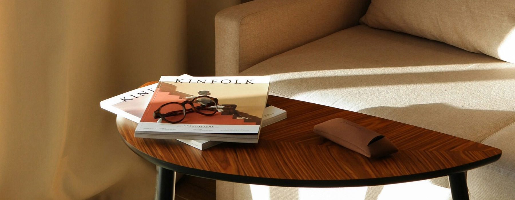 A table with a book and glasses on it next to a couch in the sunlight.
